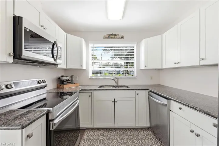 Kitchen with stainless steel appliances, white cabinets, and dark stone countertops
