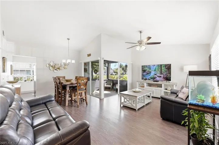 Living room with wood finished floors, vaulted ceiling, plenty of natural light, a ceiling fan, and hanging lights