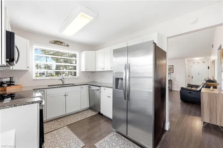 Kitchen with stainless steel appliances, dark wood-style floors, white cabinets, and dark stone counters