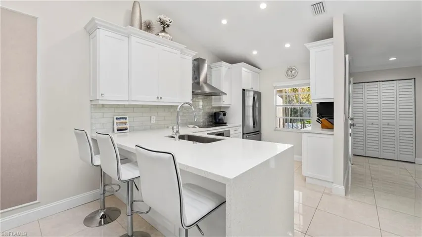 Kitchen with a kitchen breakfast bar, white cabinets, a peninsula, wall chimney range hood, and freestanding refrigerator