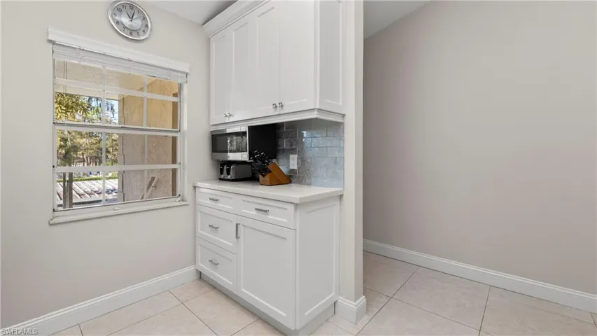 Kitchen featuring white cabinetry, tasteful backsplash, stainless steel microwave, light tile patterned floors, and light stone countertops