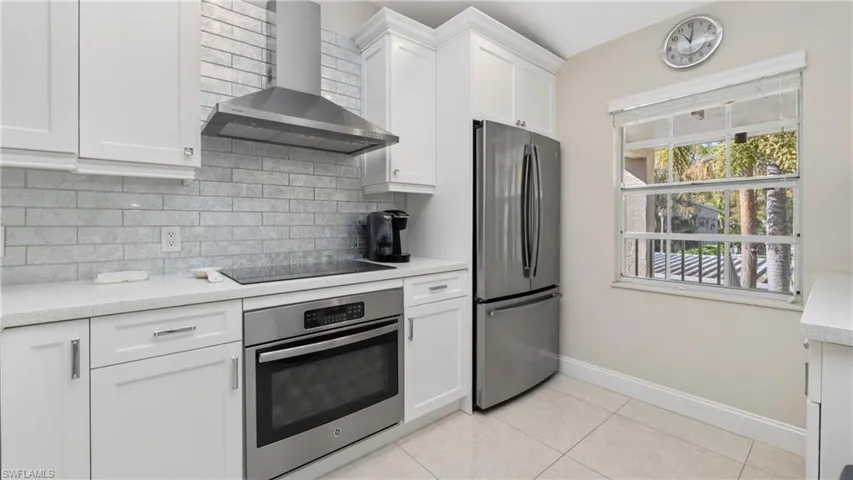 Kitchen featuring appliances with stainless steel finishes, wall chimney exhaust hood, white cabinets, light tile patterned flooring, and light stone countertops