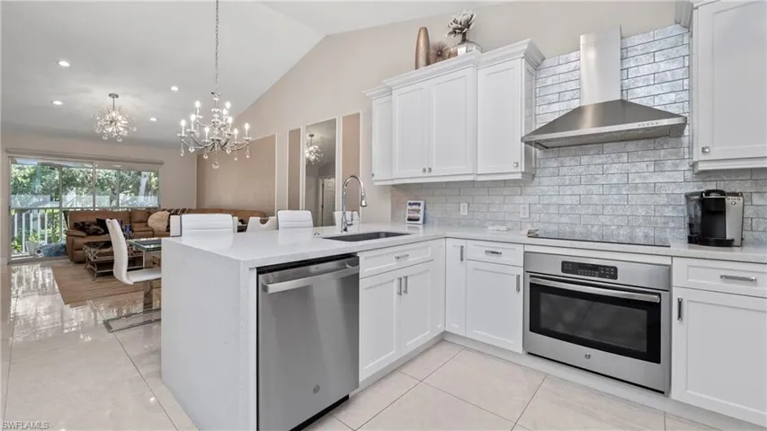 Kitchen featuring appliances with stainless steel finishes, wall chimney exhaust hood, lofted ceiling, white cabinetry, and light stone countertops