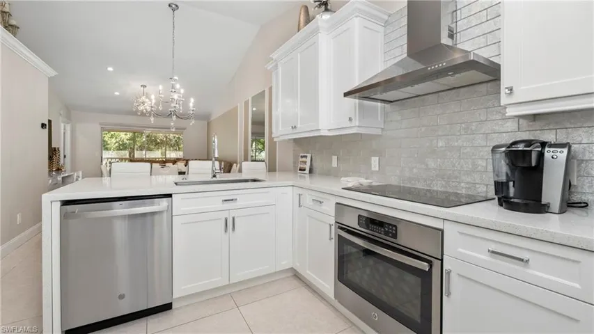 Kitchen featuring wall chimney range hood, vaulted ceiling, appliances with stainless steel finishes, a chandelier, and light stone counters