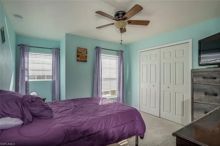 Carpeted bedroom featuring ceiling fan, multiple windows, and a closet