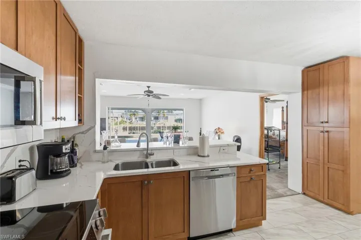 Kitchen with brown cabinetry, stainless steel appliances, a peninsula, light stone countertops, and ceiling fan