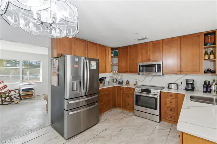 Kitchen featuring open shelves, stainless steel appliances, light stone countertops, and brown cabinets
