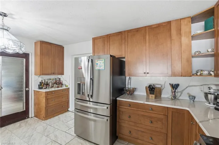 Kitchen featuring open shelves, stainless steel fridge with ice dispenser, brown cabinetry, light stone counters, and a textured ceiling