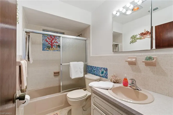 Full bath with combined bath / shower with glass door, vanity, tile walls, and a wainscoted wall