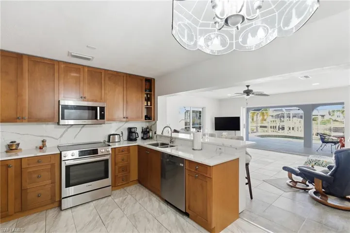 Kitchen featuring brown cabinetry, stainless steel appliances, a peninsula, tasteful backsplash, and light stone countertops