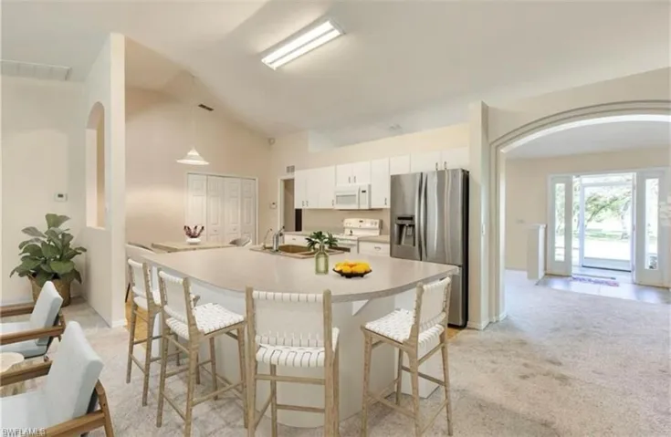 Kitchen featuring white appliances, light colored carpet, white cabinetry, a kitchen breakfast bar, and lofted ceiling