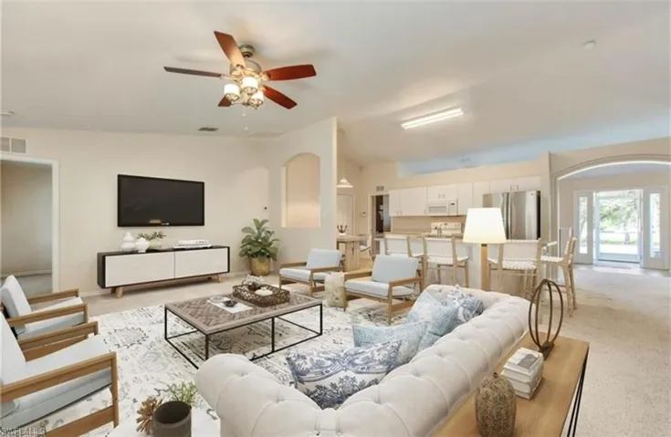 Living area with light carpet, ceiling fan, and arched walkways