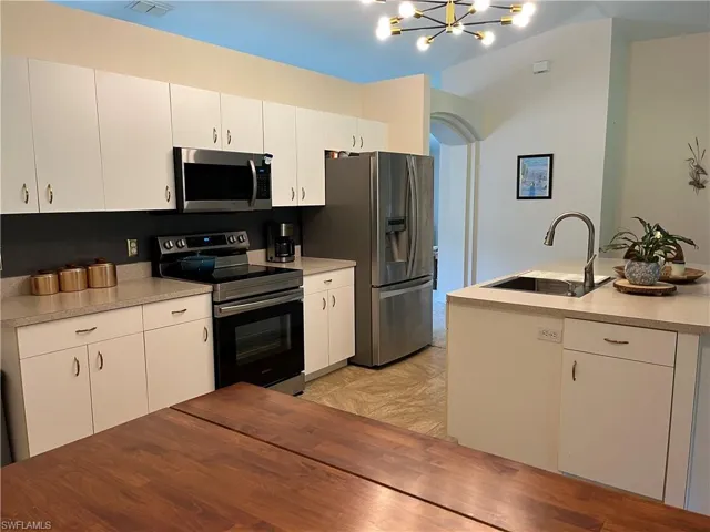 Kitchen with appliances with stainless steel finishes, a chandelier, and white cabinets