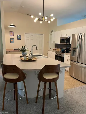 Kitchen featuring fridge, stove, a kitchen bar, white cabinetry, and high vaulted ceiling