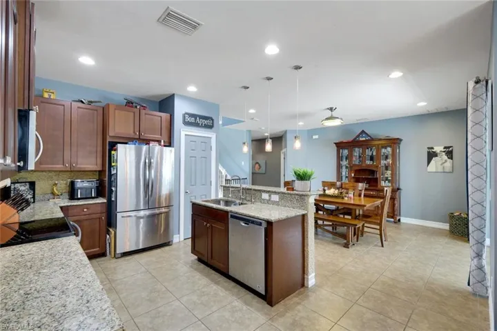 Open-concept kitchen featuring granite countertops, wood cabinetry, stainless steel appliances, and an eat-at island with pendant lighting