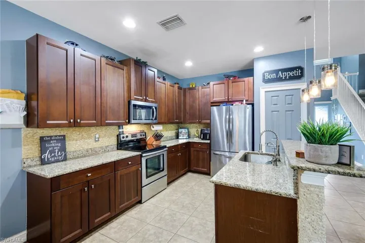 Contemporary kitchen featuring dark wood-finish cabinetry, light speckled countertops, stainless steel appliances, and a double basin sink
