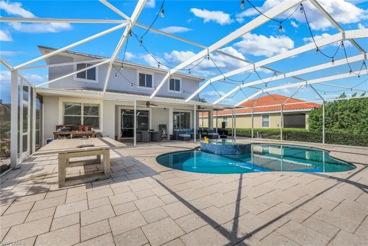 Expansive screened-in patio featuring a custom-shaped swimming pool with a mosaic-tiled spa, complemented by a surrounding paver-stone deck