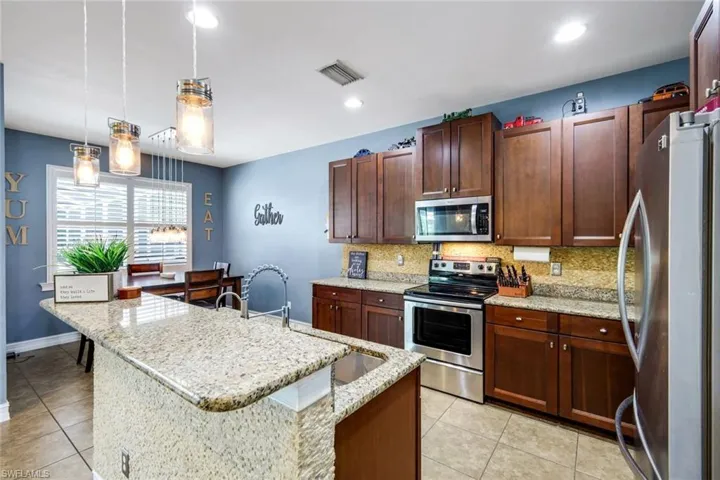 Kitchen featuring granite countertops, stainless steel appliances, dark wood cabinetry, and recessed lighting