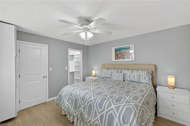 Bedroom with light wood finished floors, a textured ceiling, a walk in closet, and ceiling fan
