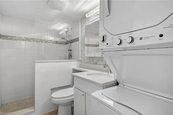 Full bathroom with a walk in shower, vanity, and stacked washer and clothes dryer
