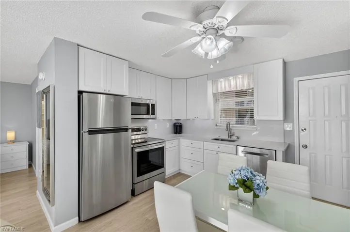 Kitchen featuring stainless steel appliances, a textured ceiling, white cabinetry, light wood-type flooring, and ceiling fan