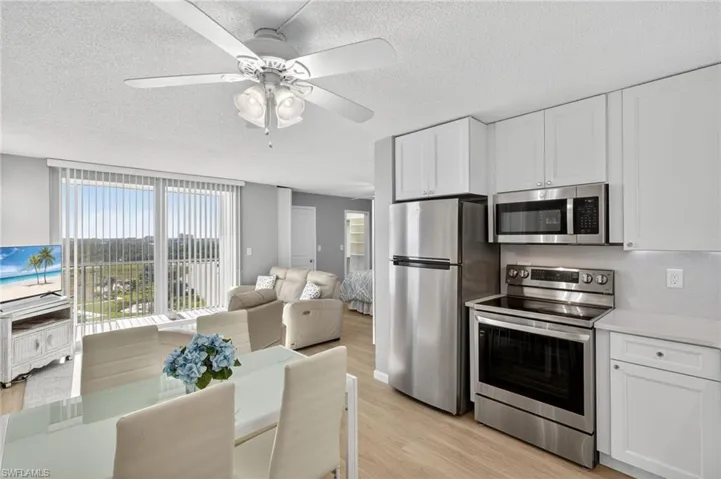 Kitchen featuring stainless steel appliances, white cabinets, light wood-style flooring, a textured ceiling, and light stone counters