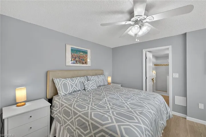 Bedroom featuring ensuite bathroom, light wood-style floors, a textured ceiling, and a ceiling fan