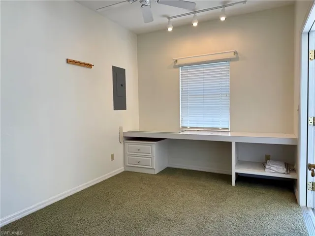 Unfurnished office with a ceiling fan, electric panel, built in desk, carpet floors, and baseboards