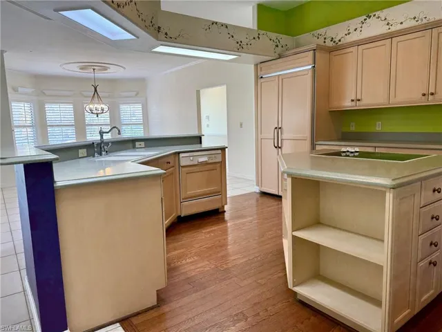 Kitchen featuring wood finished floors, paneled appliances, a large island with sink, and a sink