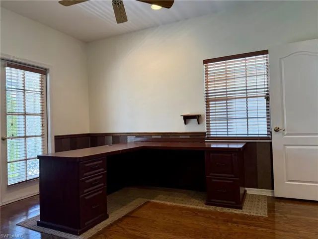 Unfurnished office with built in desk, dark wood-style flooring, and a ceiling fan