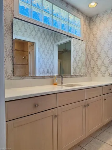 Full bathroom with tile patterned floors, a tile shower, wallpapered walls, and vanity