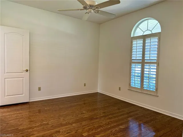 Empty room with dark wood-style floors, baseboards, and ceiling fan