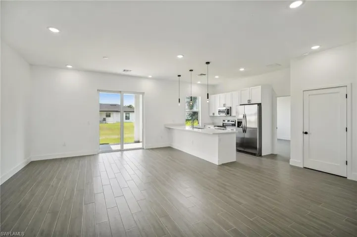 Kitchen with stainless steel appliances, hardwood / wood-style floors, white cabinetry, and pendant lighting