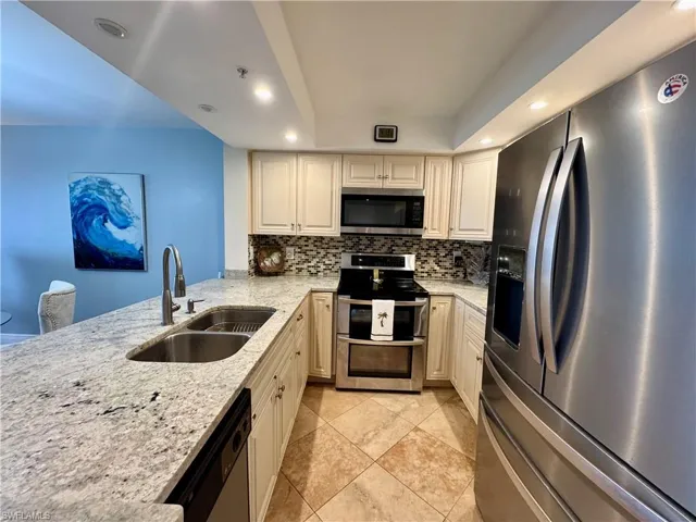 Kitchen with stainless steel appliances, sink, light stone counters, light tile patterned floors, and tasteful backsplash