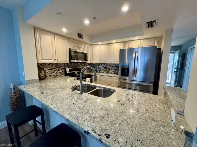 Kitchen featuring a raised ceiling, stainless steel appliances, kitchen peninsula, a kitchen bar, and sink