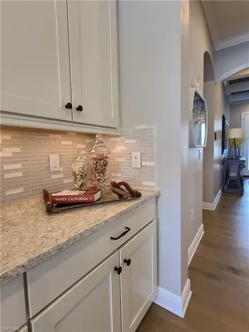 Kitchen featuring light stone countertops, white cabinetry, backsplash, and dark hardwood / wood-style flooring