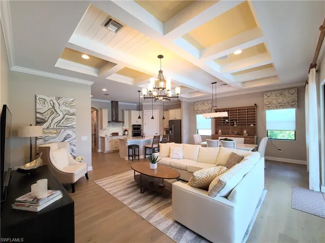 Living room featuring beam ceiling, coffered ceiling, an inviting chandelier, light wood-type flooring, and crown molding