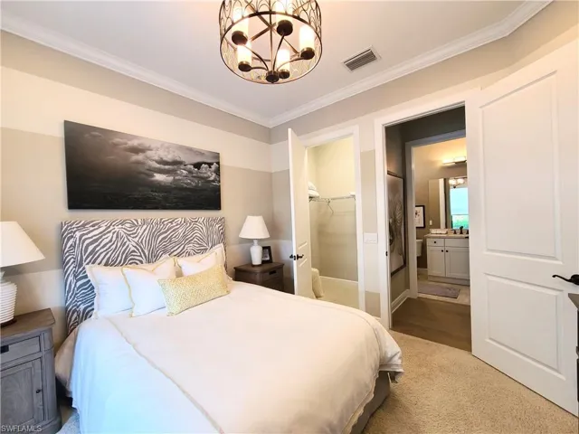 Bedroom featuring a spacious closet, a closet, crown molding, ensuite bath, and an inviting chandelier