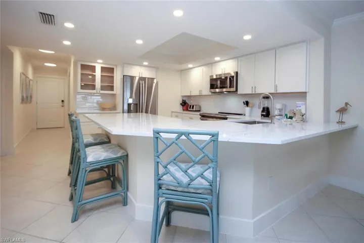 Kitchen featuring a kitchen breakfast bar, a peninsula, light stone counters, stainless steel appliances, and white cabinetry