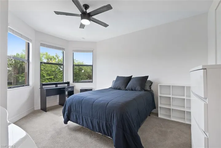 Bedroom featuring light colored carpet, multiple windows, and a ceiling fan