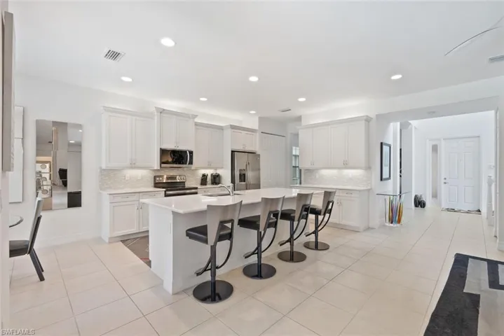 Kitchen with a breakfast bar, stainless steel appliances, light countertops, backsplash, and a kitchen island with sink