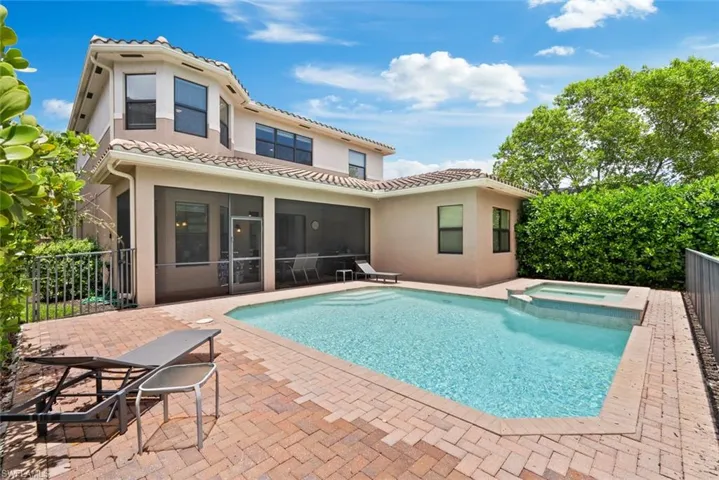 Back of property with a sunroom, stucco siding, a pool with connected hot tub, a patio, and a tile roof