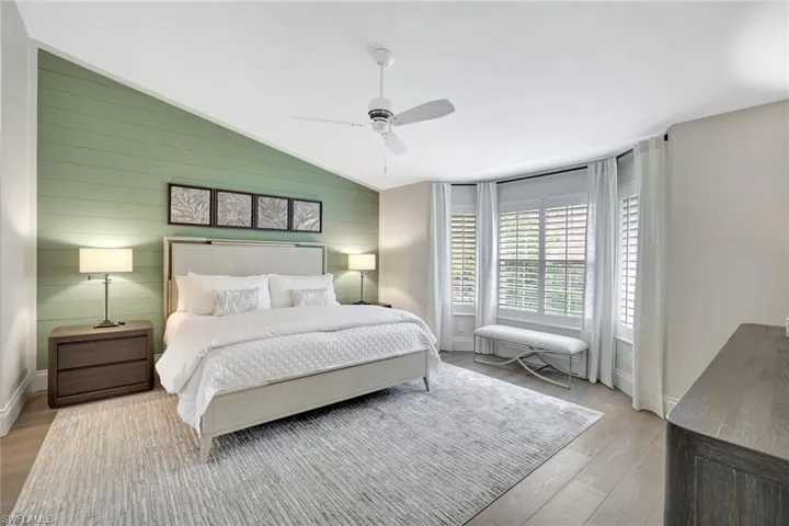 Bedroom featuring wood walls, vaulted ceiling, ceiling fan, and wood finished floors