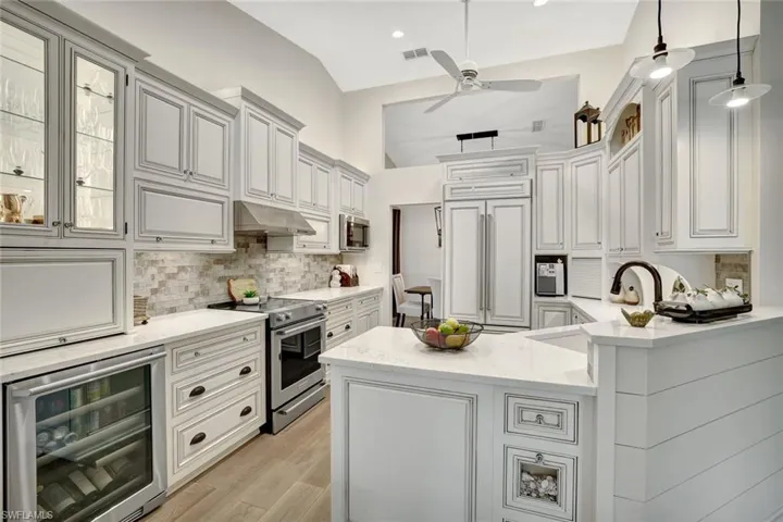 Kitchen with wine cooler, stainless steel appliances, light stone counters, a peninsula, and under cabinet range hood