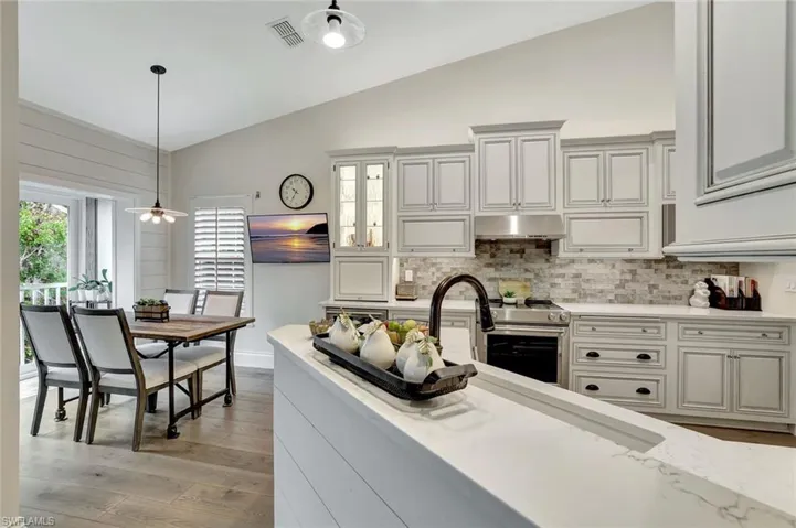 Kitchen with light stone counters, hanging light fixtures, lofted ceiling, stainless steel range, and tasteful backsplash