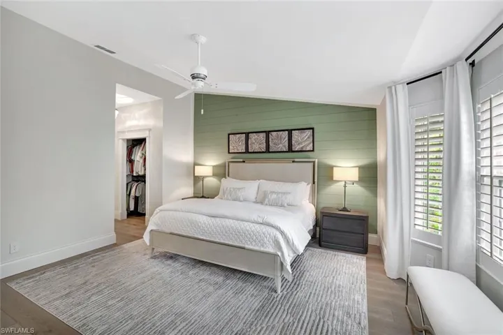 Bedroom featuring vaulted ceiling, a ceiling fan, wooden walls, wood finished floors, and a walk in closet