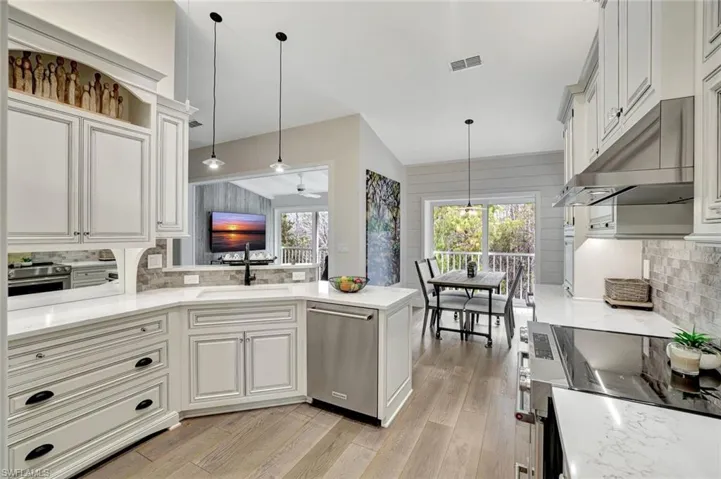 Kitchen with tasteful backsplash, appliances with stainless steel finishes, decorative light fixtures, and under cabinet range hood