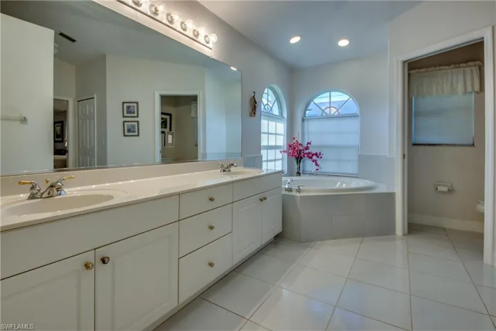Bathroom with a relaxing tiled tub, vanity, tile patterned flooring, and toilet