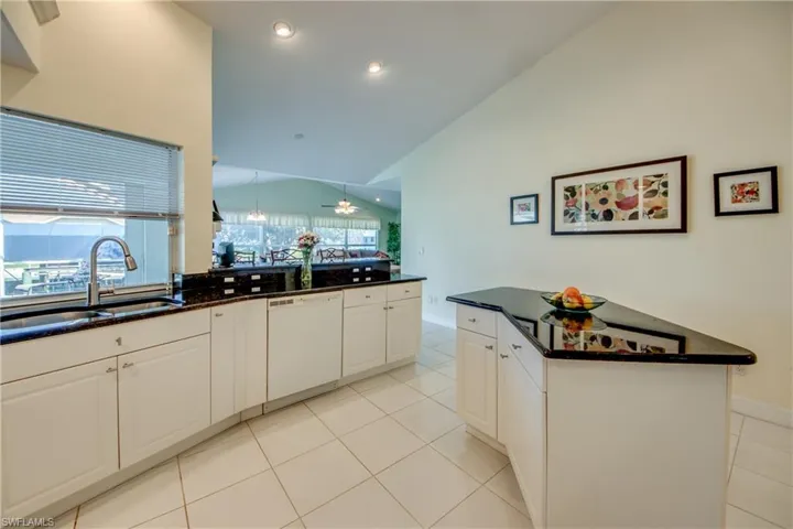 Kitchen featuring lofted ceiling, sink, light tile patterned floors, dishwasher, and white cabinets