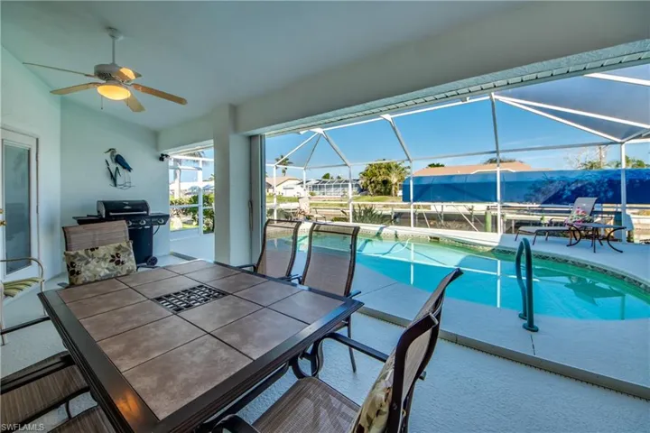 View of swimming pool with ceiling fan, area for grilling, glass enclosure, and a patio area